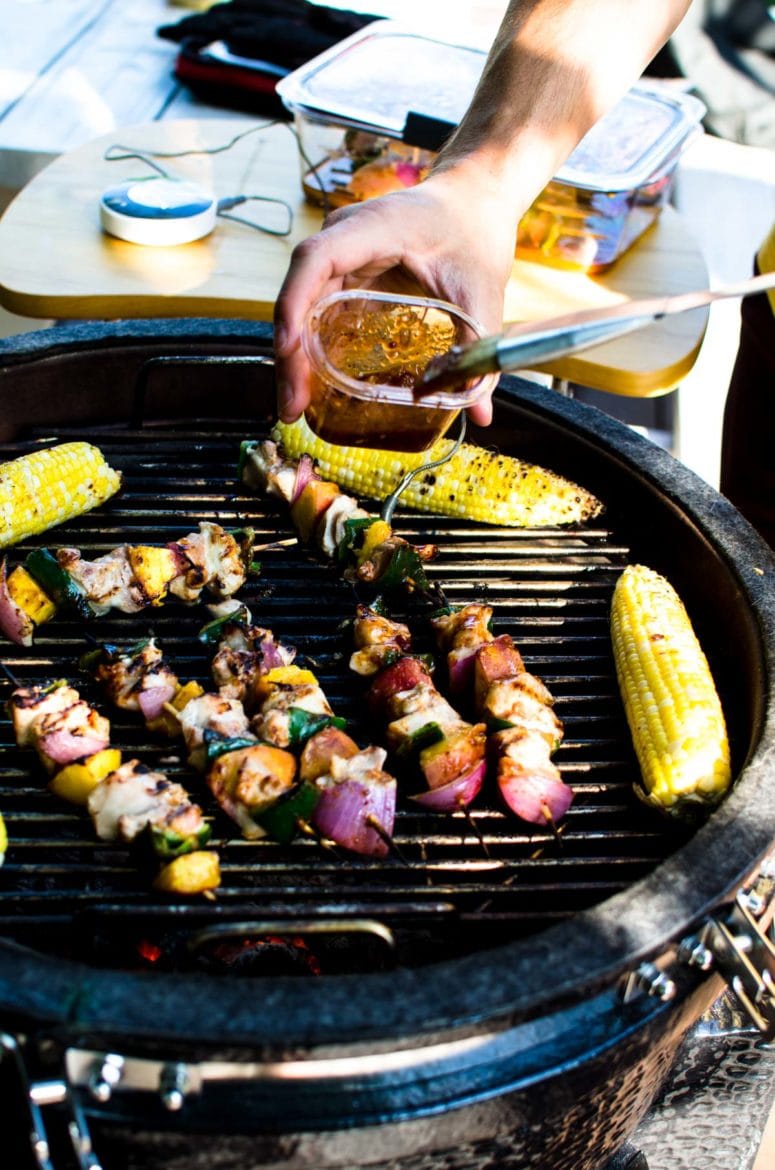 An open grill with peach bbq chicken kabobs and grilled corn on the grill grates.