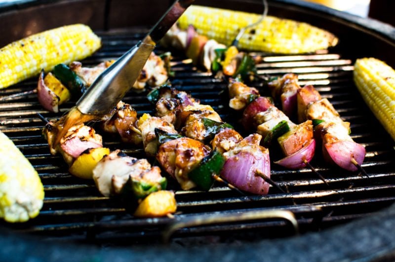 An open grill with a marinade brush brushing sauce on Peach BBQ Chicken kabobs. 