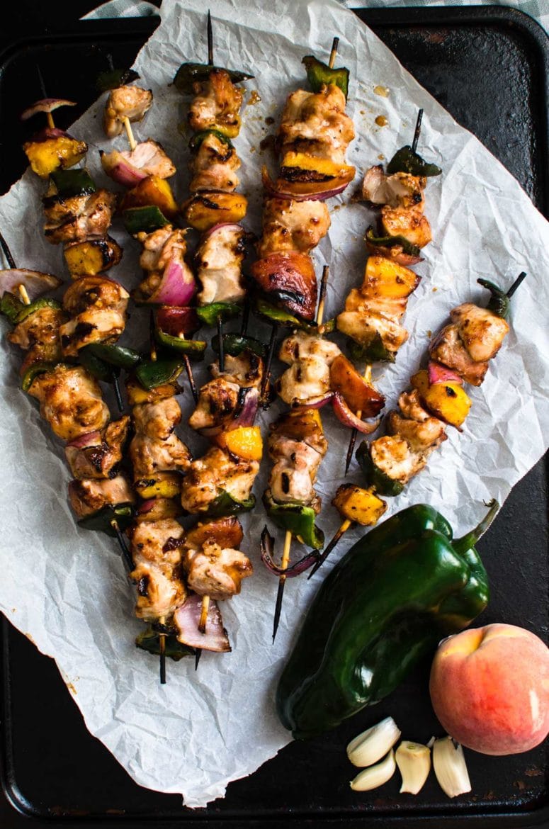 Overhead shot of peach bbq chicken kabobs on a piece of white parchment paper against a metal baking tray. 