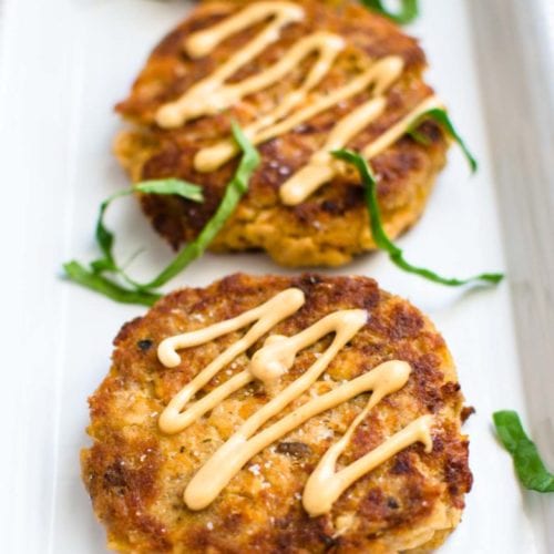 A white platter with salmon cakes garnished with aioli.