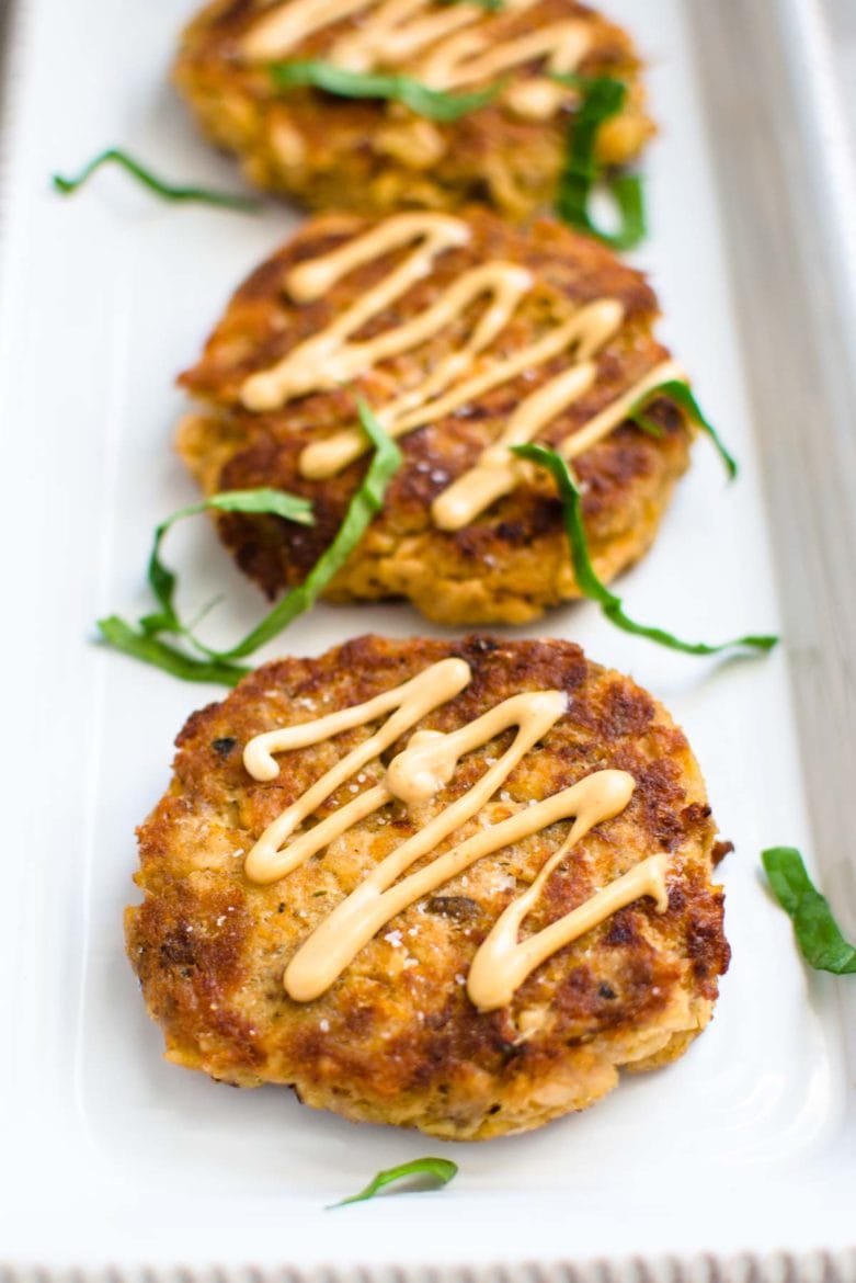 A white platter with salmon cakes garnished with aioli. 