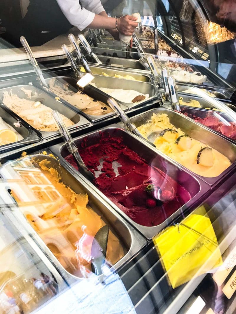 Gelato serving shop with many flavors shown.