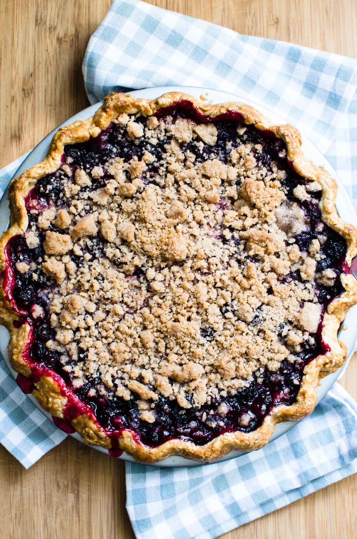 Mixed berry crumble pie just out of the oven on a wood board.