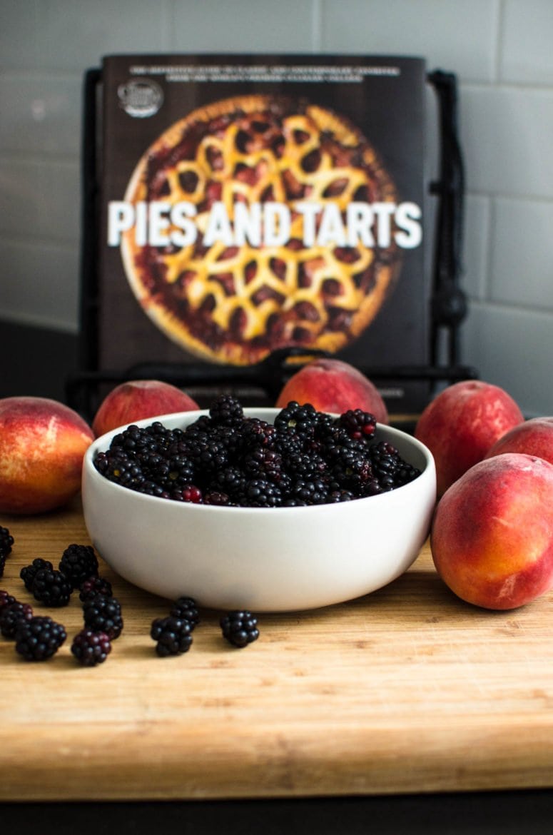 Bowl of blackberries surrounded by peaches with cookbook in background.