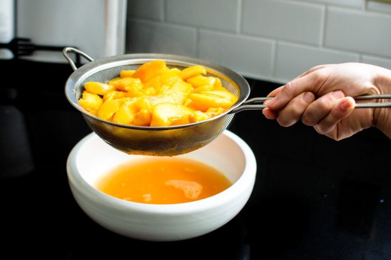 Sliced peaches in a colander being drained over a bowl. 
