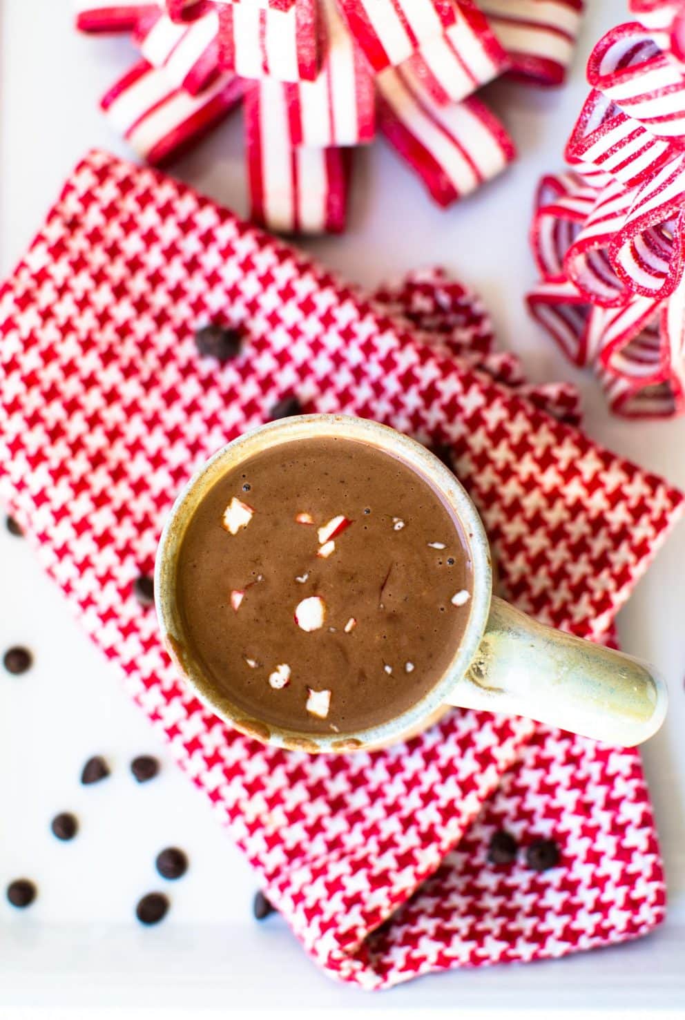 A mug of hot chocolate agains a red plaid dish towel with candy cane trees in the background.