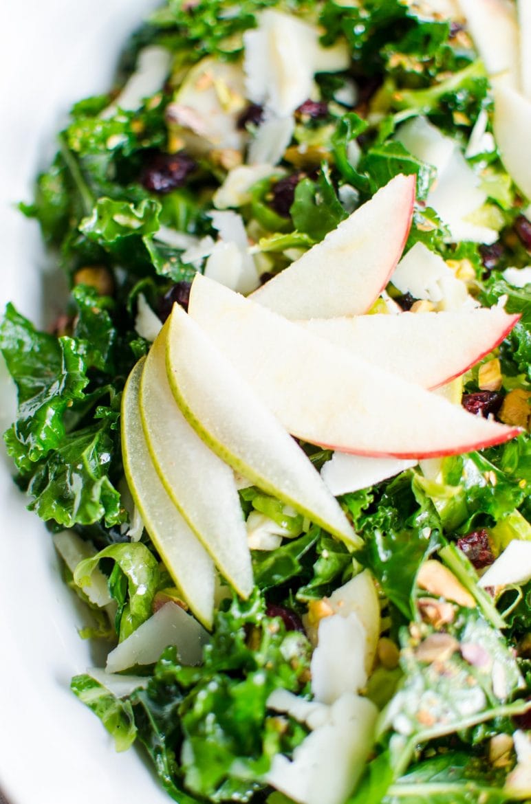 Close-up shot of a kale salad with pear and apple garnish fanned over the top of the salad. 