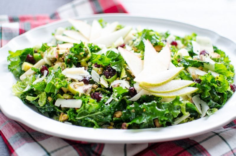 Side shot of a kale salad on a white platter with fanned apple slices garnishing the top. 