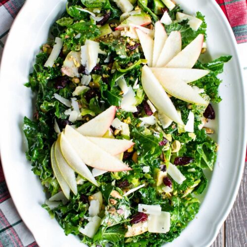 A festive kale salad with Brussels sprouts, apples, cranberries, pistachios, Parmesan, and a sweet + tangy apple cider vinaigrette. Tips on how to style a salad for a holiday party.