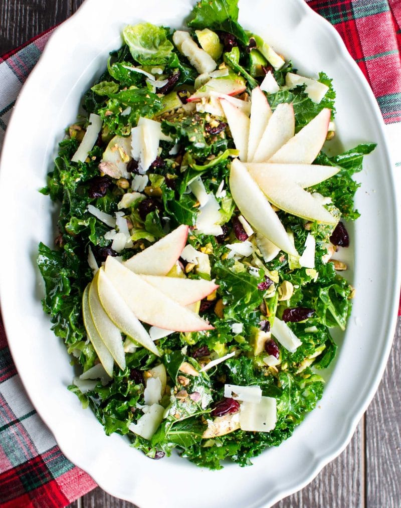 A kale and apple salad on a large white platter with a plaid holiday towel in the background. 