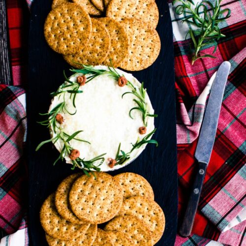 A pesto cheesecake Christmas wreath on a slate serving board with crackers on the side.