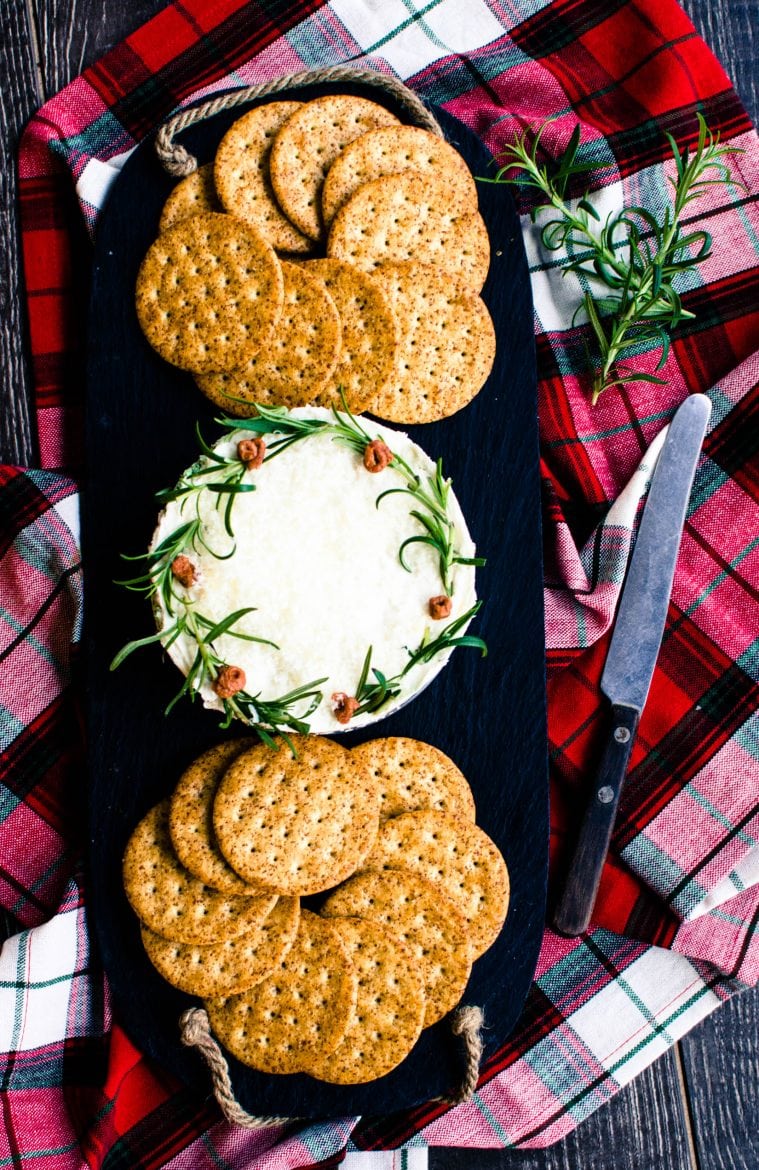 A pesto cheesecake Christmas wreath on a slate serving board with crackers on the side. 