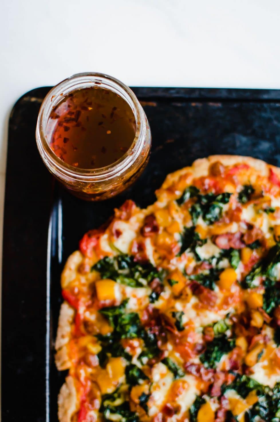 A butternut squash pizza on a baking sheet with a jar of hot honey in the corner. 