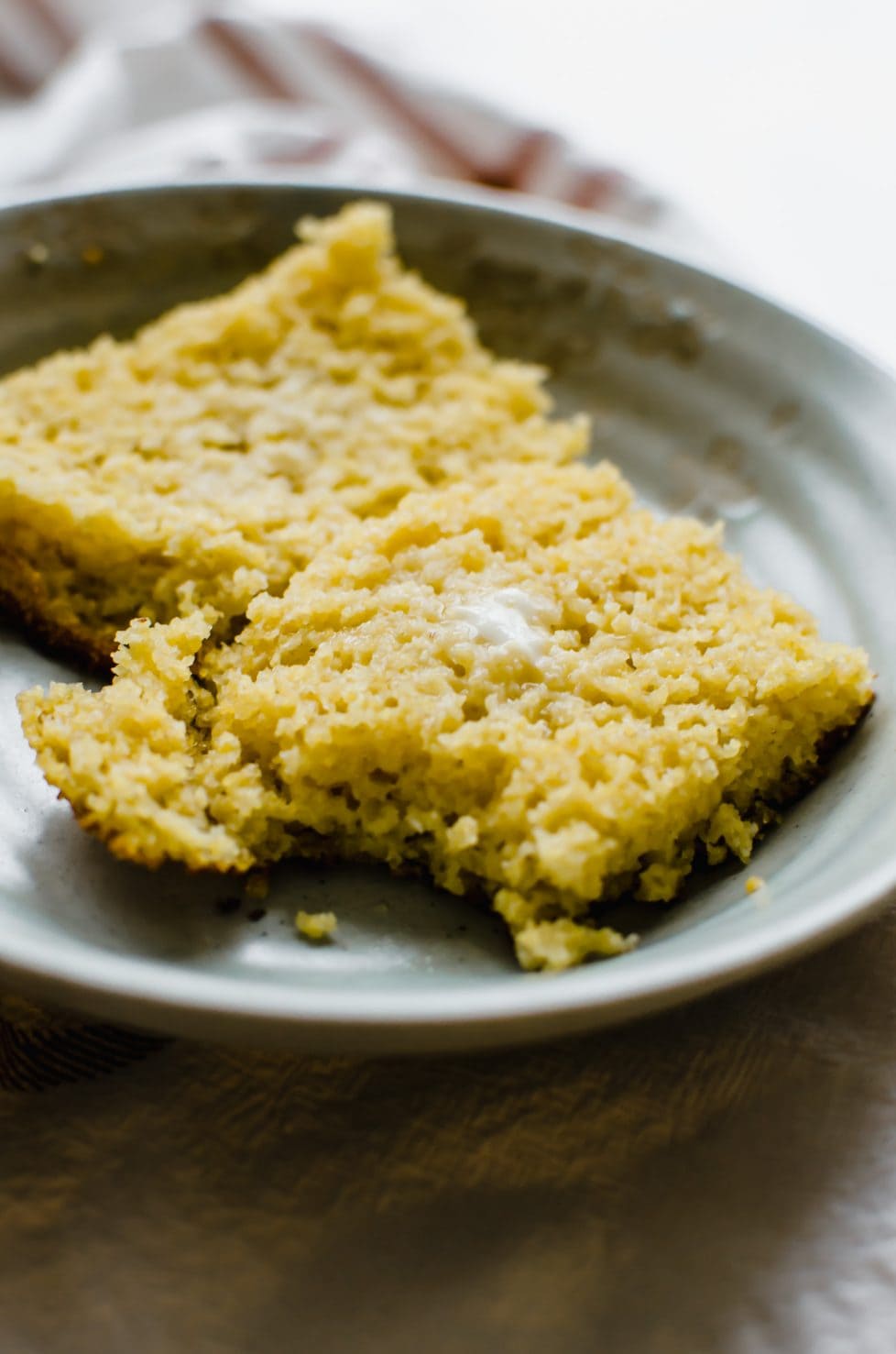 A slice of cornbread cut in half and topped with butter. 