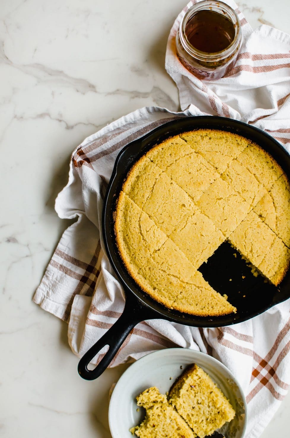 Overhead view of cast iron skillet with cornbread and a jar of honey.