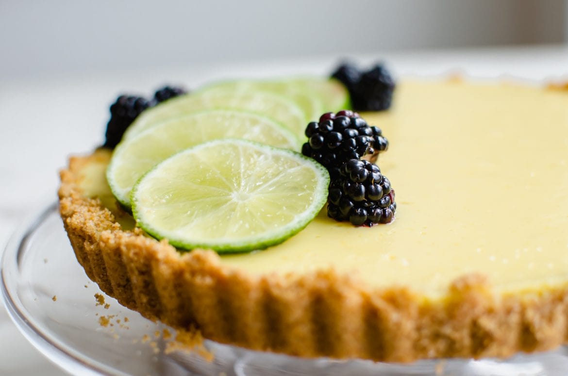 This recipe for a fresh lime tart has a buttery graham cracker crust and beautiful fresh blackberry sauce on top. It is very easy to make and would be perfect for St. Patrick's Day or Easter! #baking #sweetcayenne