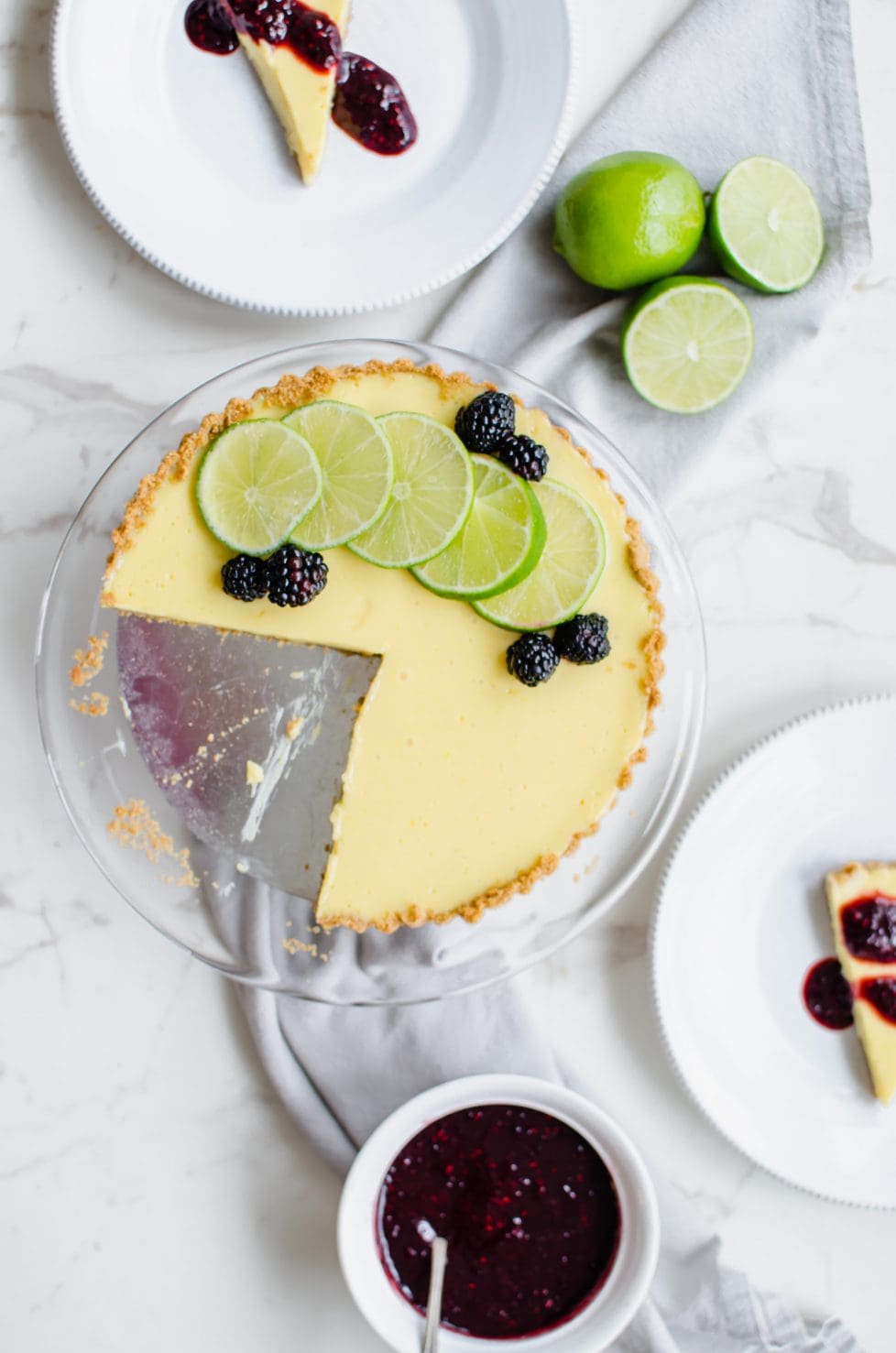 A lime tart on a cake platter with plates of sliced lime tart on the side. 