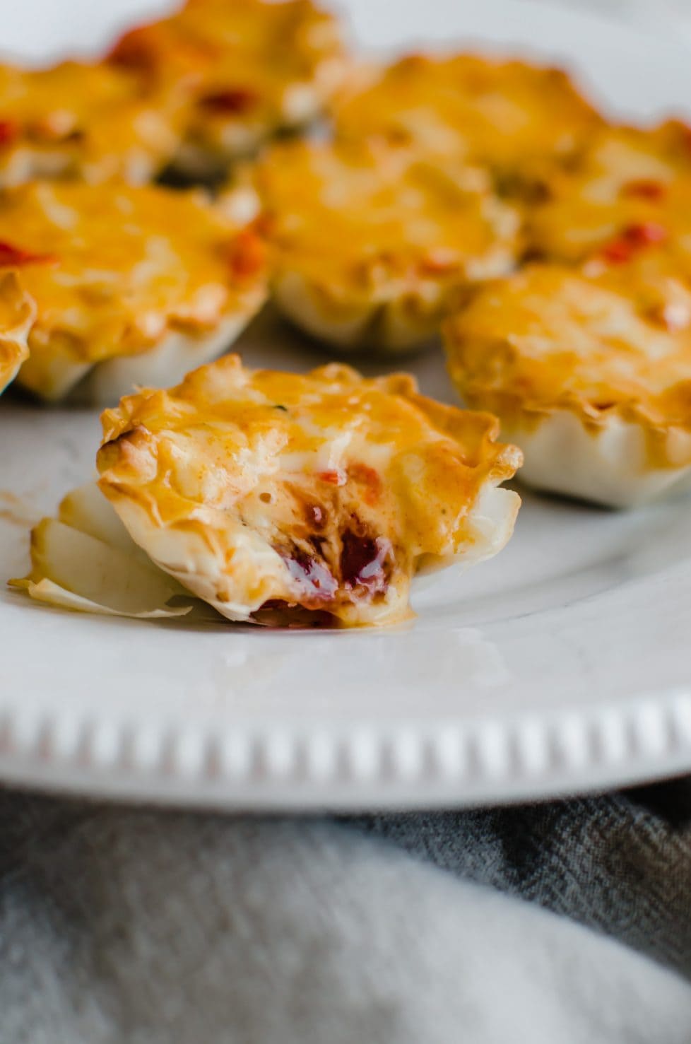 Close up view of a pimento cheese tartlet with a bite of out if.