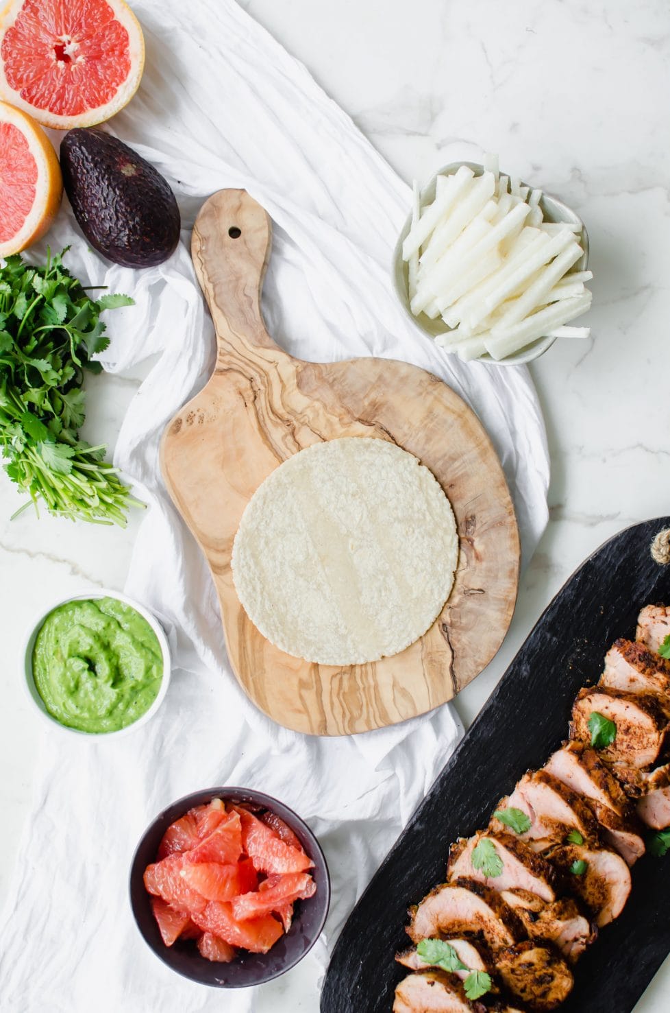 Olive wood cutting board with a corn tortilla and other tacos fillings. 