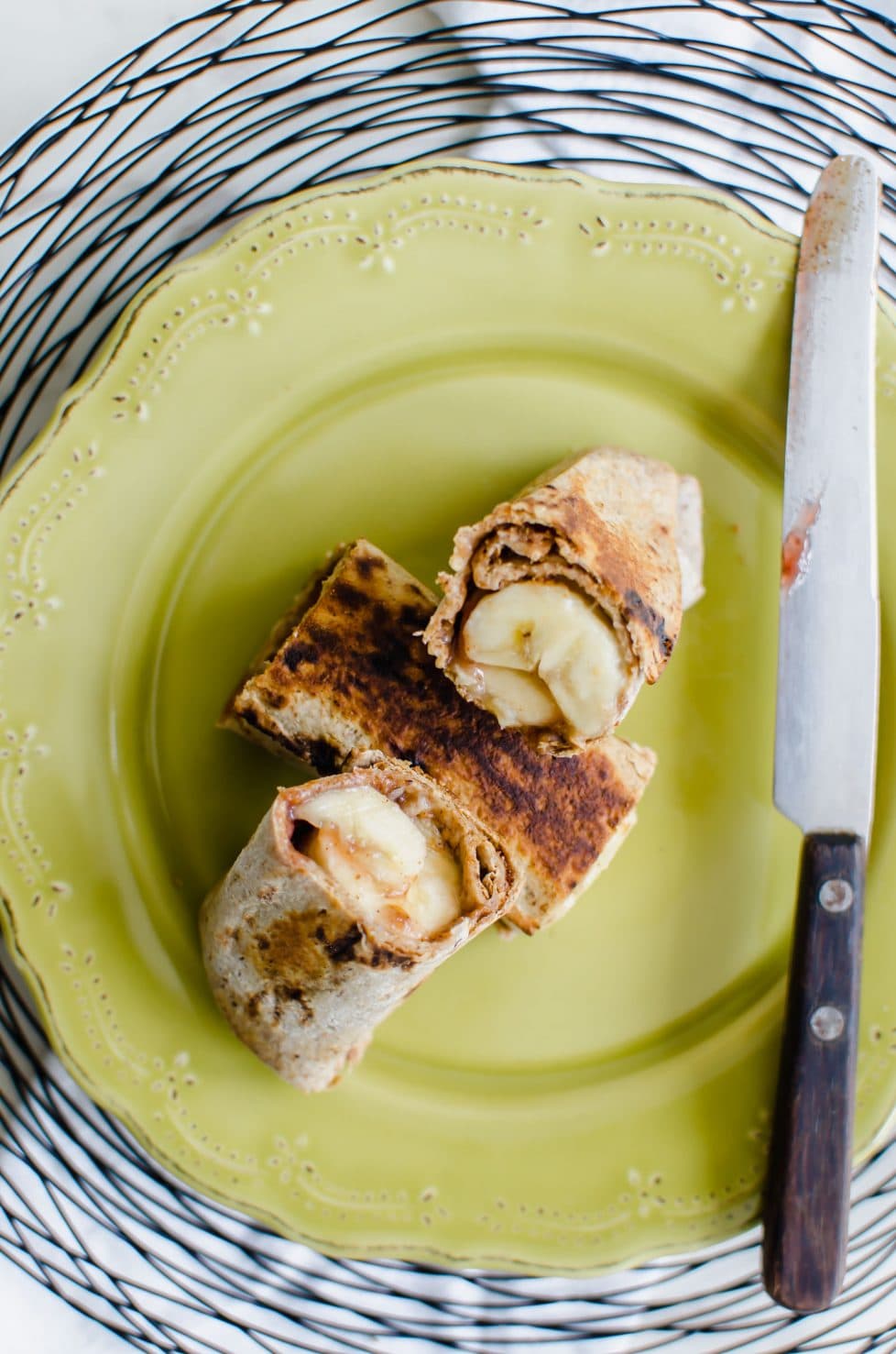 A sliced almond butter banana chimichanga on a green plate with a jelly knife on the side. 