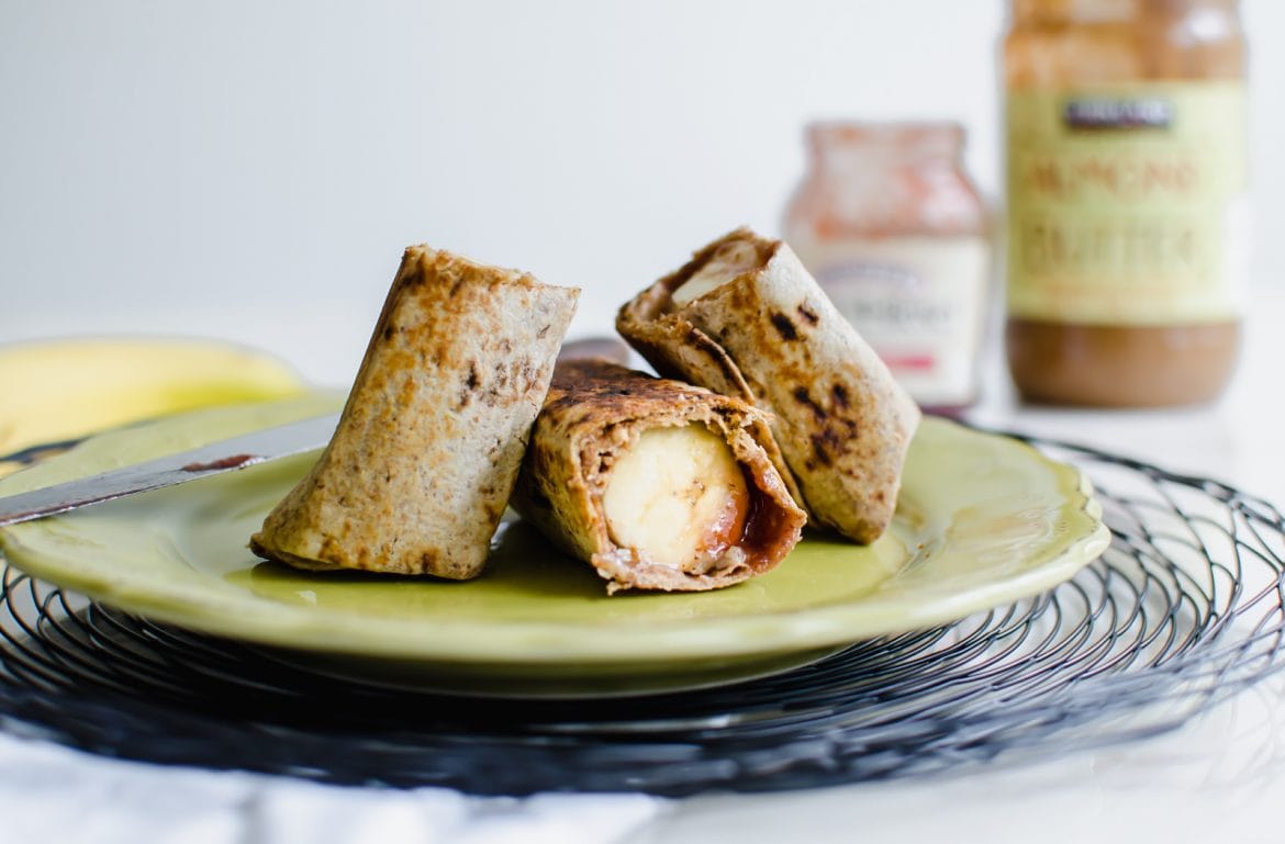 Straight-on shot of a whole grain wrap with a banana, almond butter, and jam inside sitting on a green plate.