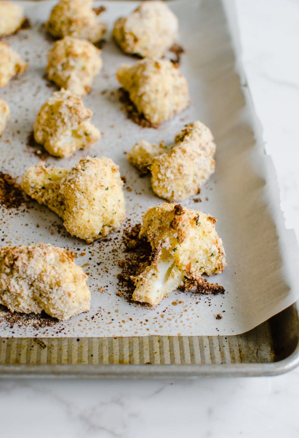 A close-up of a piece of breaded baked cauliflower on a baking sheet. 