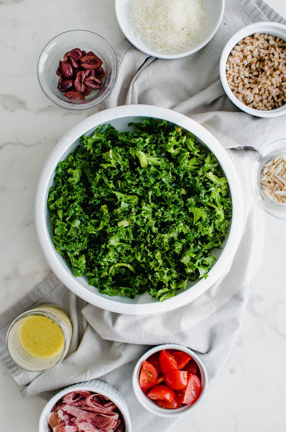 A bowl of kale with different salad ingredients seen in other containers.