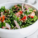 Overhead side photo of Italian Kale salad topped with veggies and sliced meat.