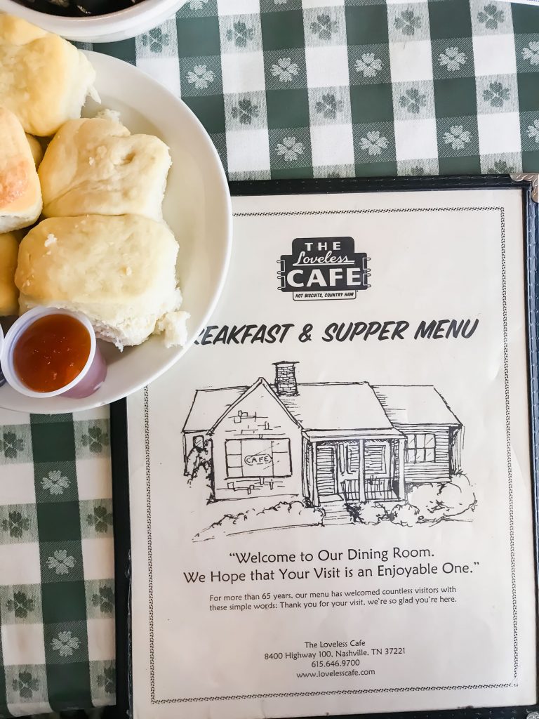 A menu for the Loveless Cafe sitting on a checkerboard tablecloth with a plate of biscuits to the side.