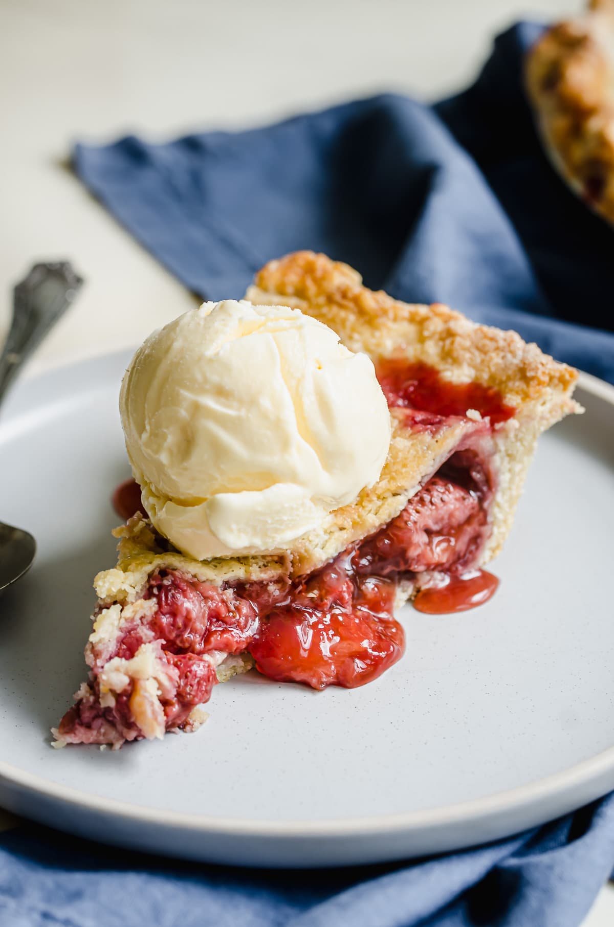 A double crust slice of strawberry pie topped with ice cream.