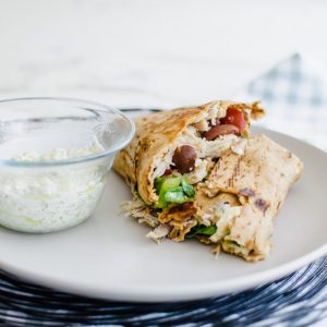 Greek crunch wrap sliced in two pieces on a plate with dipping sauce.