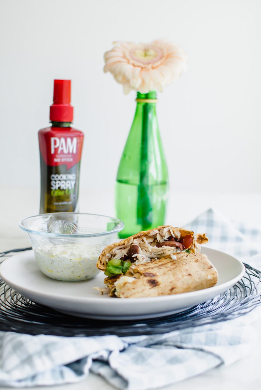 A white plate with a Greek Chicken Crunchwrap sliced in half and a bowl of feta dipping sauce.