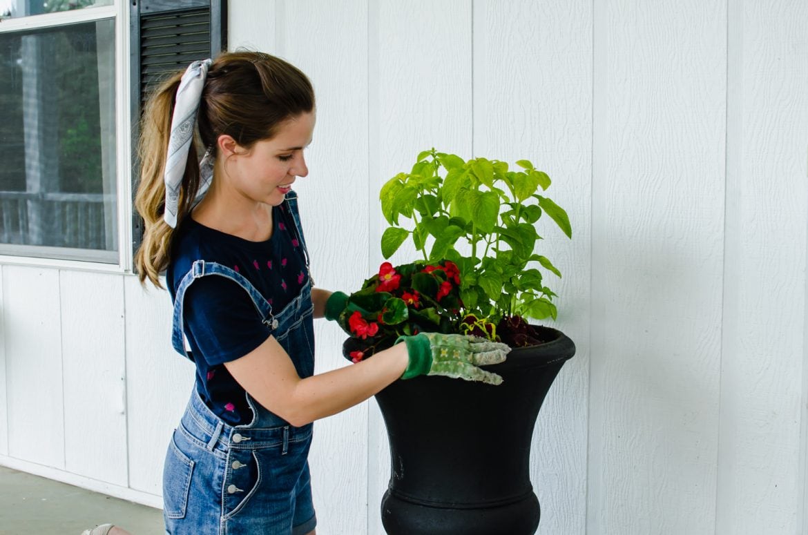 A straight-on shot of a girl with gardening gloves on planting flowers in a black pot.