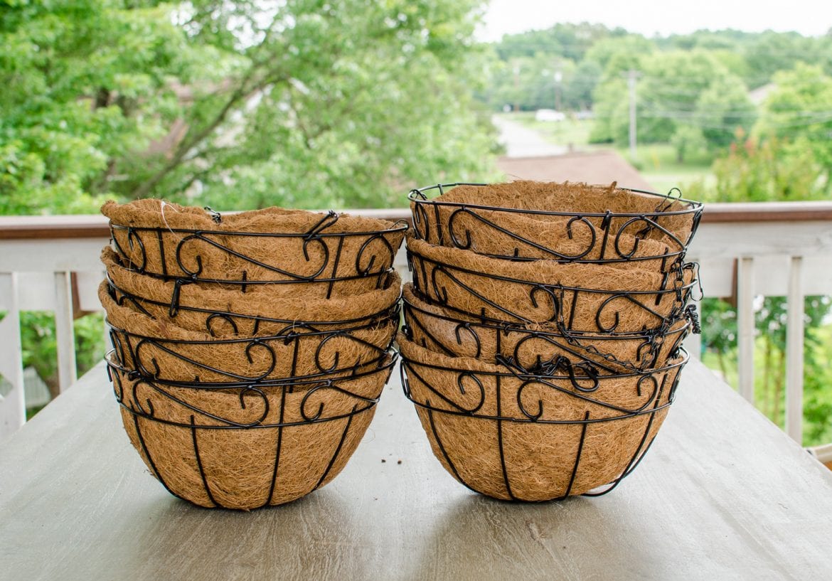 Two stacks of black iron hanging flower baskets on a gray table.