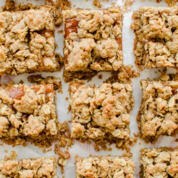 An overhead shot of Pecan Butter and Peach Jam Crumble Bars sitting on white parchment paper.