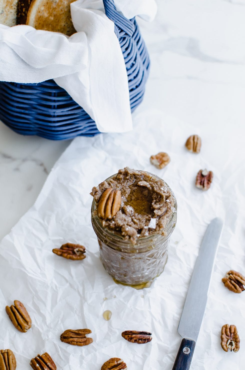 An overhead shot of a mason jar with maple pecan butter inside. The top is garnished with a pecan halve and some sea salt flakes.