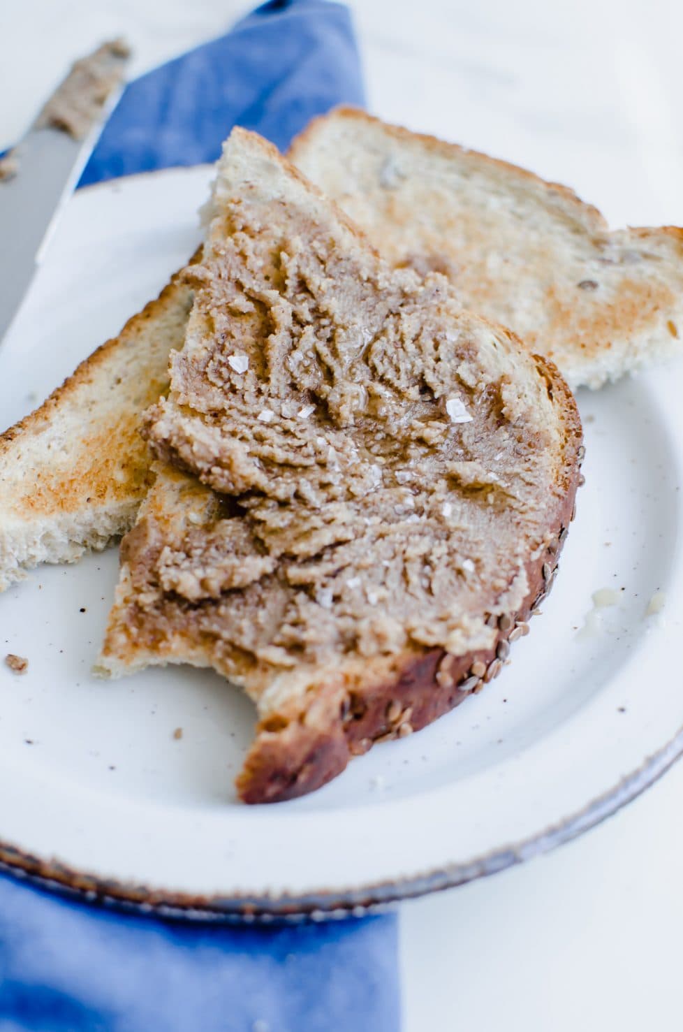 An overhead shot of a slice of toast with pecan butter on top and some sea salt plates. The toast is on a white plate. 