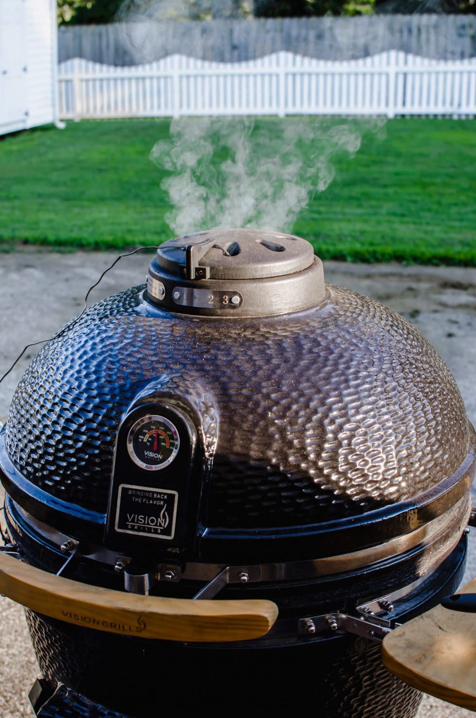 A shot of the top of a kamado grill with smoke coming out of the top vent.