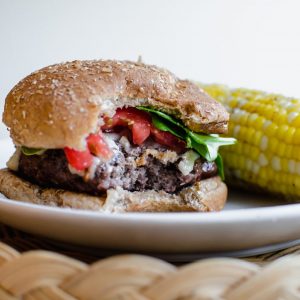 A burger topped with spinach and tomato with a bite taken out of it and an ear of corn on the side.