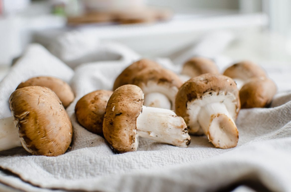 A horizontal shot of raw baby bella mushrooms on a light gray kitchen towel.