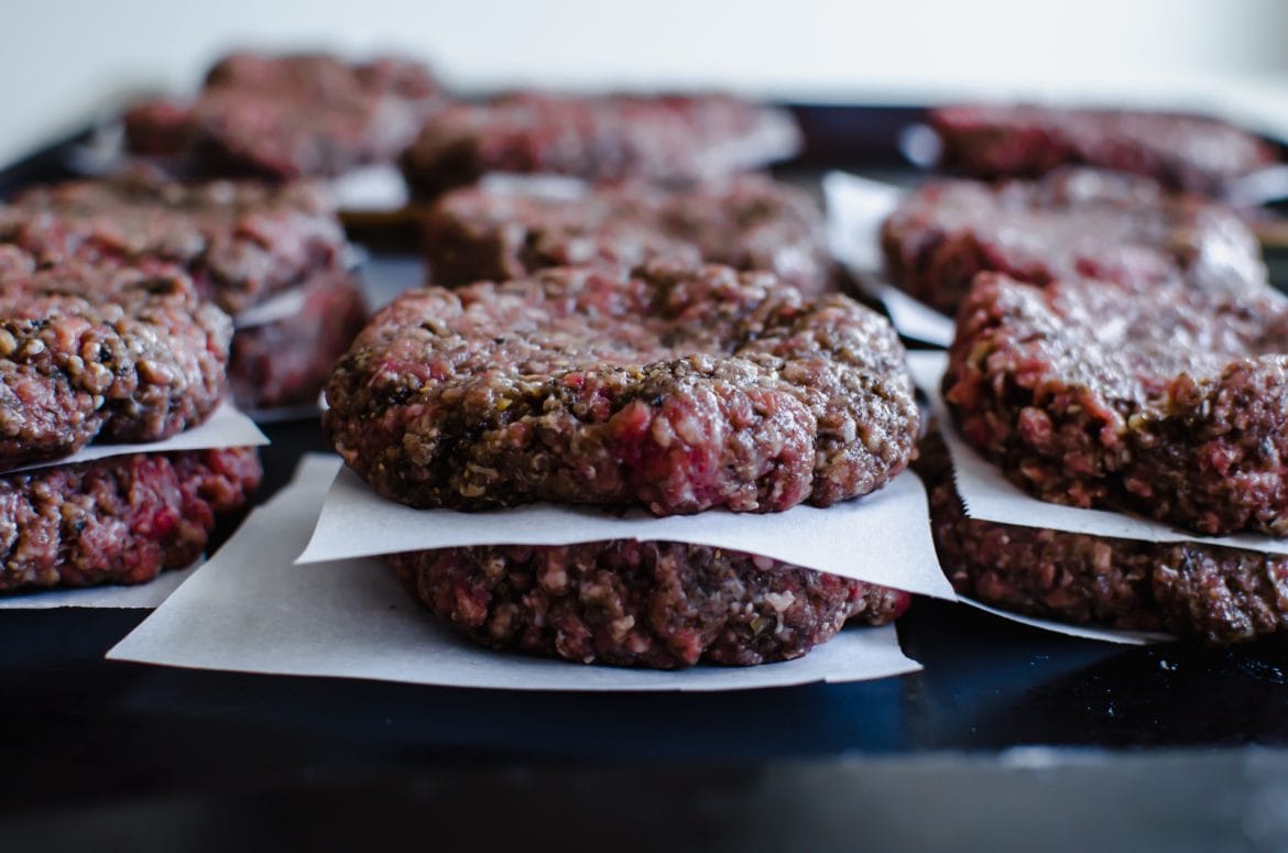 A horizontal shot of a pan of hamburger patties stacked two to stack with parchment paper in between the patties. 