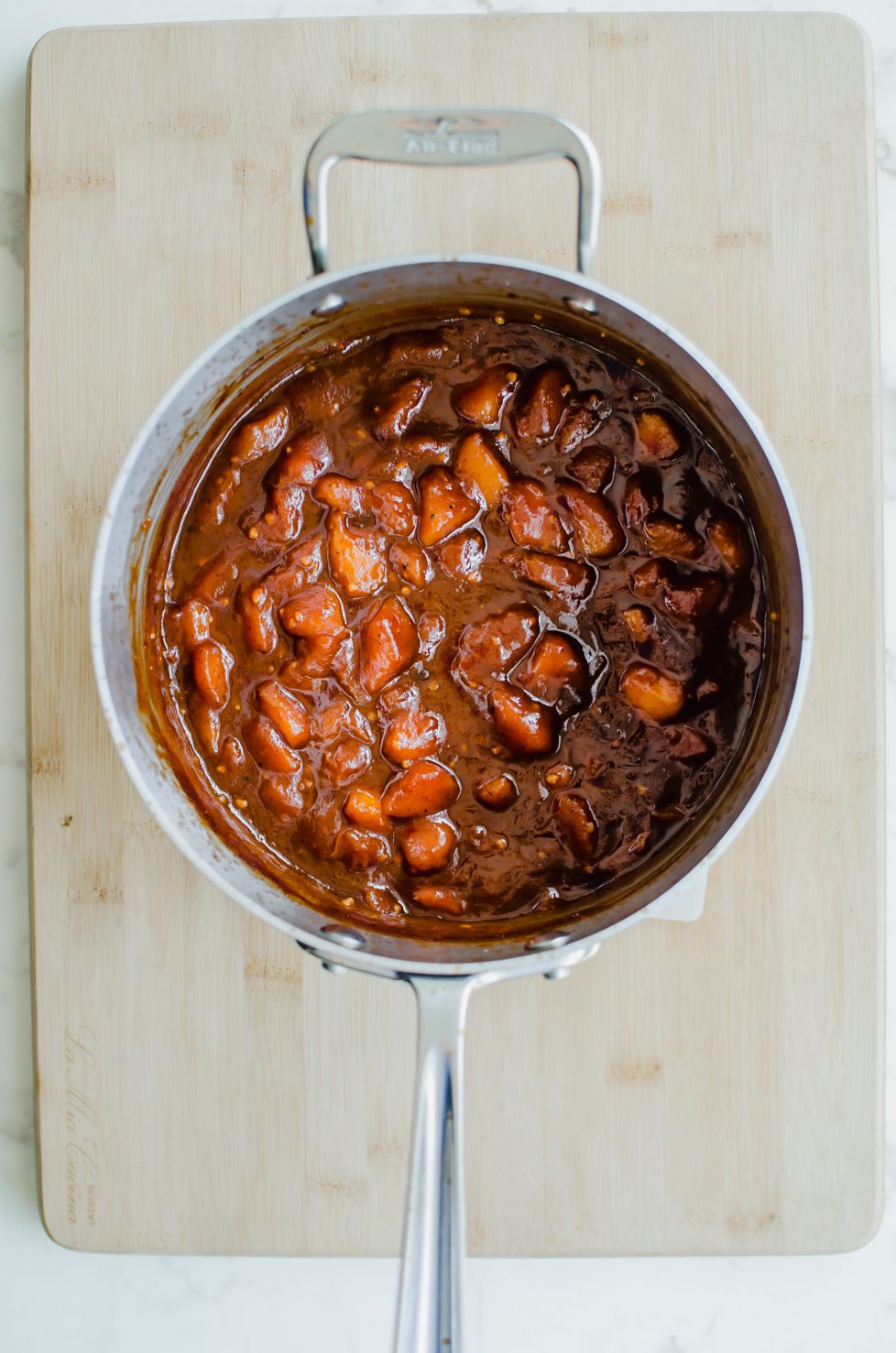 An overhead shot of a large saucepan filled with peach bourbon bbq sauce sitting on a white marble countertop.