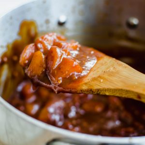 A close-up shot of a spoon over a saucepan with a scoop of peach bourbon bbq sauce.