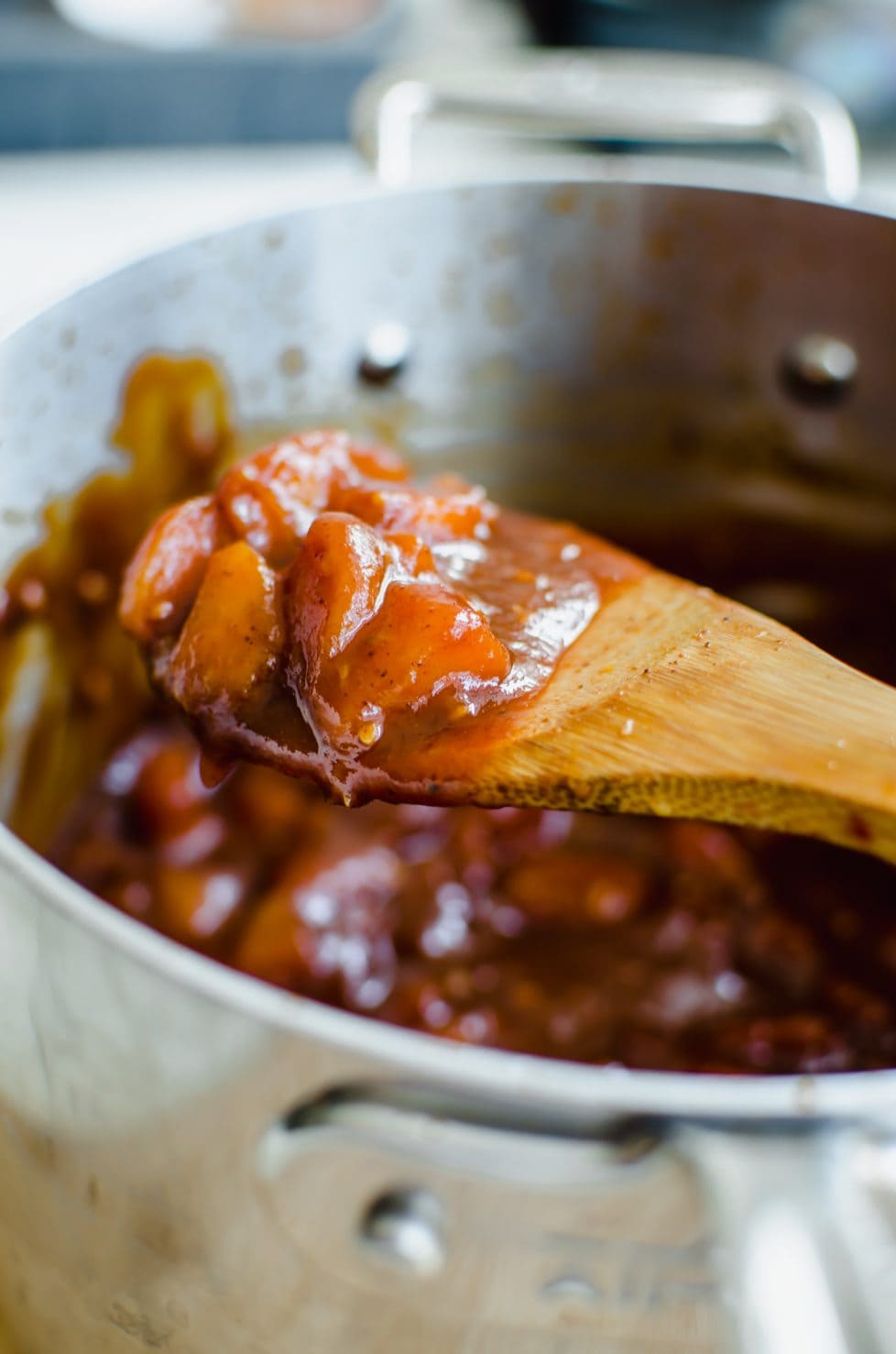 A close-up shot of a spoon over a saucepan with a scoop of peach bourbon bbq sauce. 