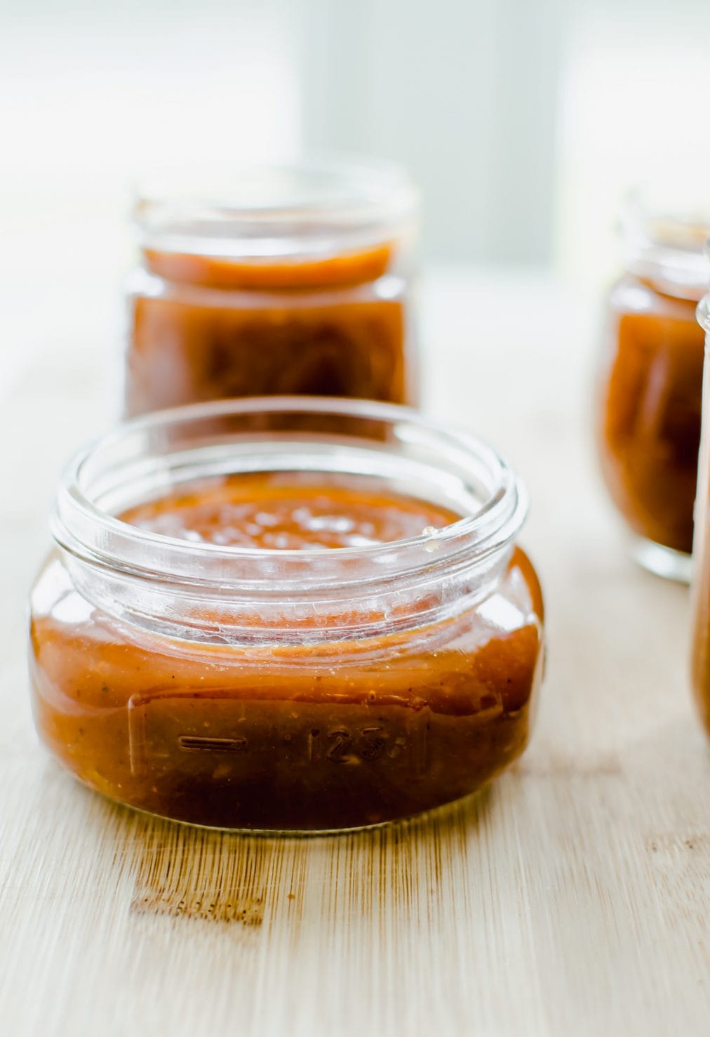 A close up of a canning jar filled with peach bourbon bbq sauce against a white background. 