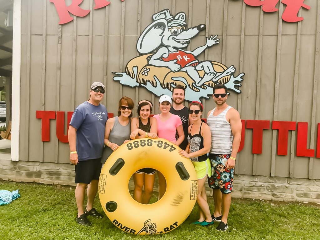 A family with a yellow inflated tube in front of the Smoky Mountain River Rat sign.