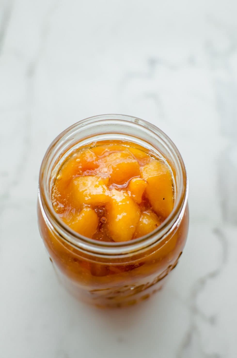 An overhead shot of an open jar of peach jam. 