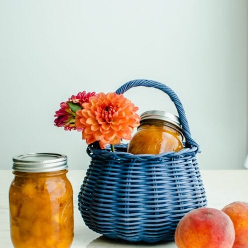 A shot of a blue wicker basket filled with dahlias and a jar of homemade peach jam.
