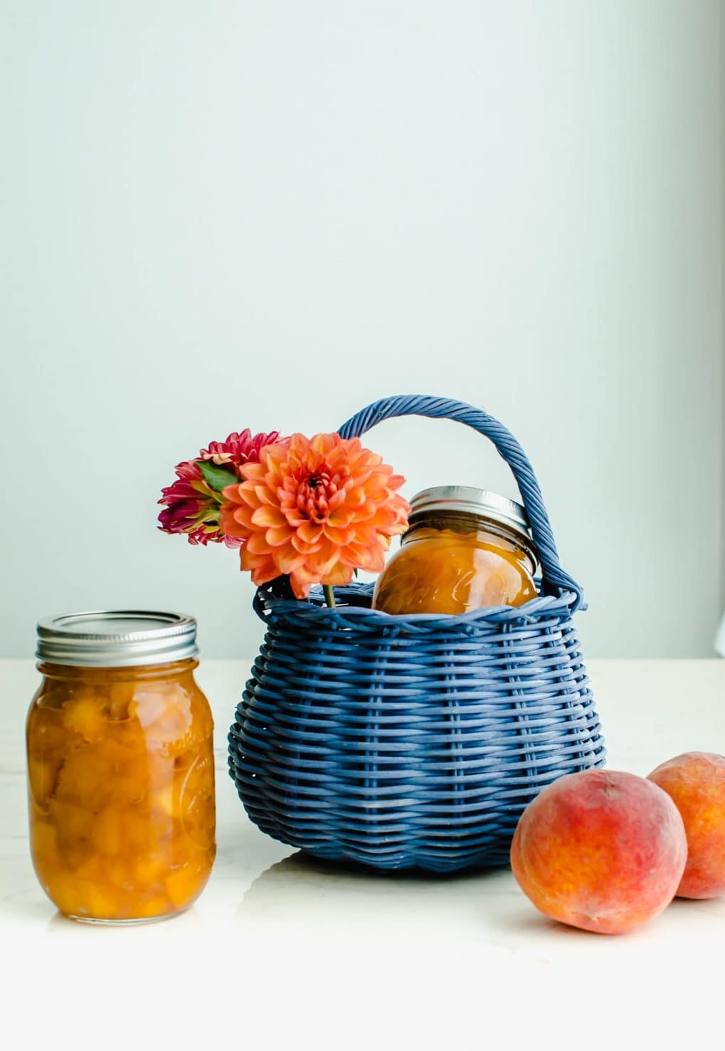 A shot of a blue wicker basket filled with dahlias and a jar of homemade peach jam.