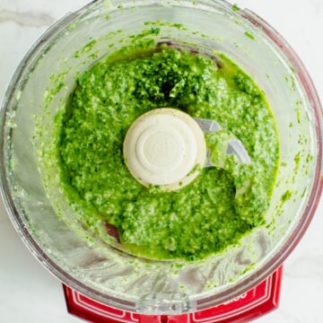 An overhead shot of a food processor with basil pesto inside.